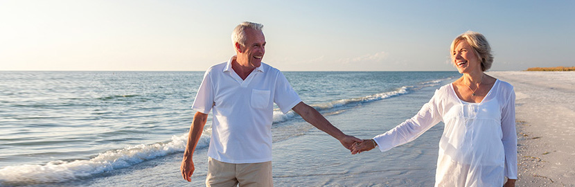 Mann und Frau spazieren Hand in Hand am Strand beim sonnigen Wetter