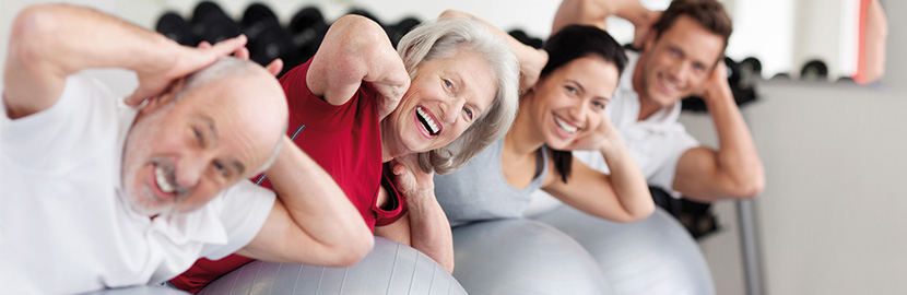 Zwei Männer und zwei Frauen liegen auf Sportbälle im Fitnessraum