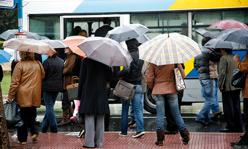 Menschen mit Regenschirmen vor einem Bus