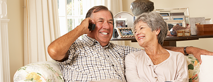 Gebührenfrei erreichbar! Senior Frau und Senior Mann am Telefon sitzen nebeneinander auf dem Sofa im Wohnzimmer